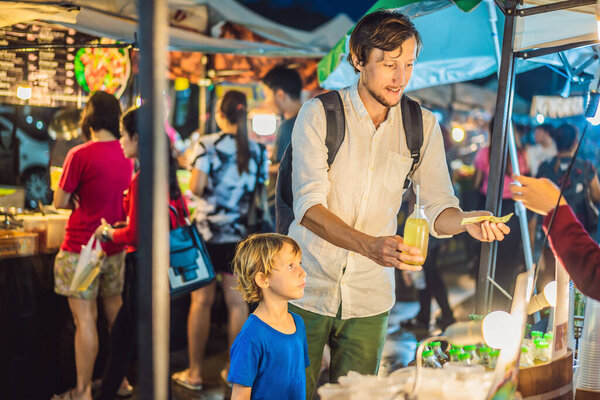 Coronavirus is over. Quarantine weakened. Take off the mask. Now you can go to public places. Dad and son are tourists on Walking street Asian food market