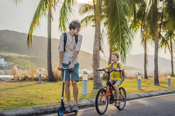 Aktivní školák a jeho otec jezdí na kole s batohem za slunečného dne. Šťastné dítě na kole na cestě do školy. Bezpečný způsob pro děti venku do školy — Stock fotografie