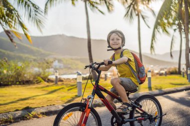 Güneşli bir günde sırt çantasıyla bisiklet süren kasklı okul çocuğu. Okula giderken mutlu çocuk bisikleti. Çocuklar için güvenli okul yolu.