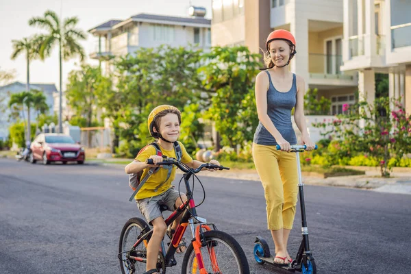 Active school kid boy and his mom in safety helmet riding a bike with backpack on sunny day. Happy child biking on way to school. Safe way for kids outdoors to school