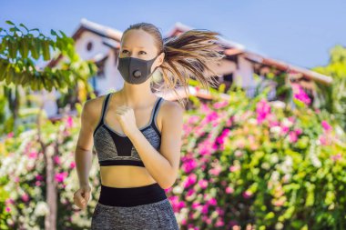 Tıbbi maske takan bir kadın koşucu. Parkta koşmak. Coronavirus salgını Covid-19. Spor, karantinada aktif yaşam yüz maskesi korumalı cerrahi sterilizasyon. Atletizm pistinde açık hava koşusu