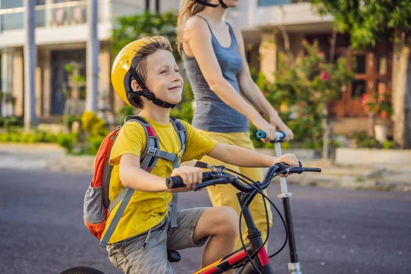 Aktivní školák a jeho máma v bezpečnostní helmě na kole s batohem za slunečného dne. Šťastné dítě na kole na cestě do školy. Bezpečný způsob pro děti venku do školy — Stock fotografie