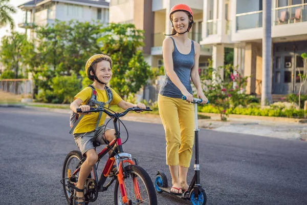 Активный школьник и его мама в защитном шлеме катаются на велосипеде с рюкзаком в солнечный день. Счастливый ребенок едет в школу на велосипеде. Безопасный способ для детей на открытом воздухе в школу — стоковое фото