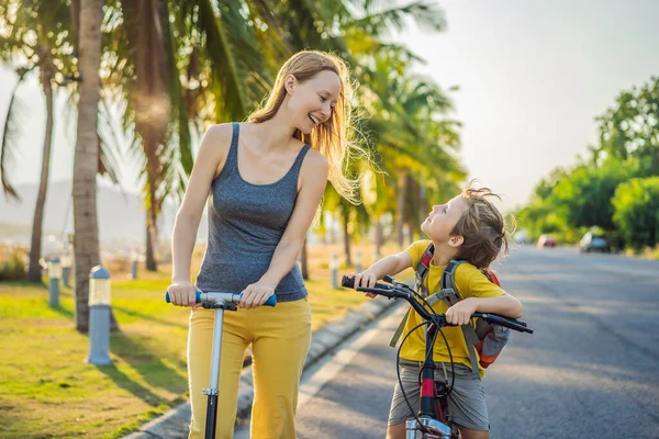 Bambino della scuola attiva e sua madre in bicicletta con lo zaino nella giornata di sole. Bambino felice in bicicletta sulla strada per la scuola. Modo sicuro per i bambini all'aperto a scuola — Foto Stock