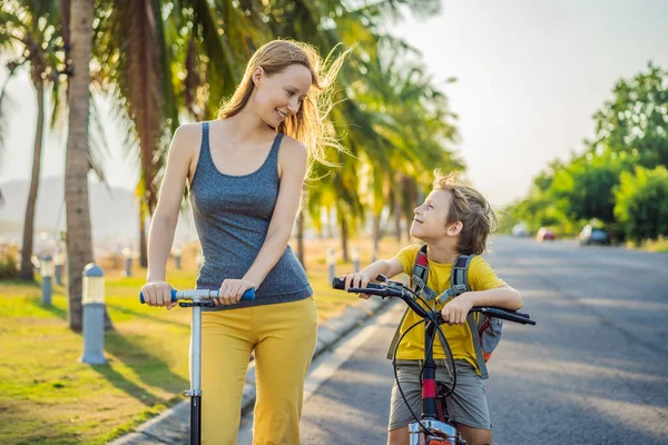 Активный школьник и его мама едут на велосипеде с рюкзаком в солнечный день. Счастливый ребенок едет в школу на велосипеде. Безопасный способ для детей на открытом воздухе в школу — стоковое фото