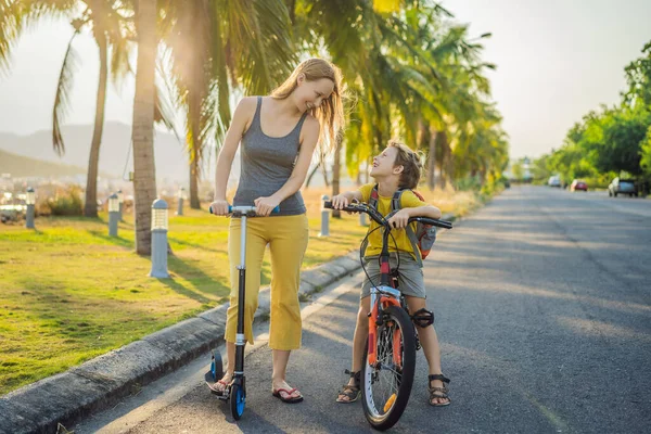 Aktiv skolpojke och hans mamma åker cykel med ryggsäck på solig dag. Glad barncykel på väg till skolan. Säkert sätt för barn utomhus till skolan — Stockfoto