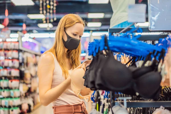 Женщина в магазине одежды в медицинской маске из-за короновируса. Карантин закончился, теперь ты можешь пойти в магазин одежды. — стоковое фото