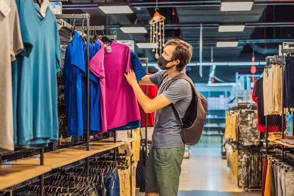 Man in a clothing store in a medical mask because of a coronovirus. Quarantine is over, now you can go to the clothing store