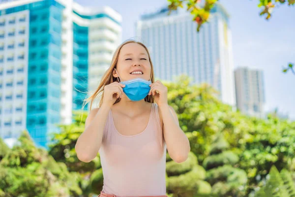 Quarantine is over concept. Woman taking off mask against the background of small town houses. We are safe. Coronavirus ended. We won. No more quarantine. Breathe deep. Take off the mask — Stock Photo, Image