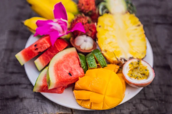 Colorful tropical fruits on big plate. On rustic wooden background. Top view — Stock Photo, Image