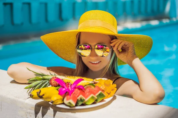 Jovem relaxante e comendo prato de frutas na piscina do hotel. Dieta de verão exótica. Foto de pernas com comida saudável à beira da piscina, vista superior de cima. Estilo de vida tropical na praia — Fotografia de Stock