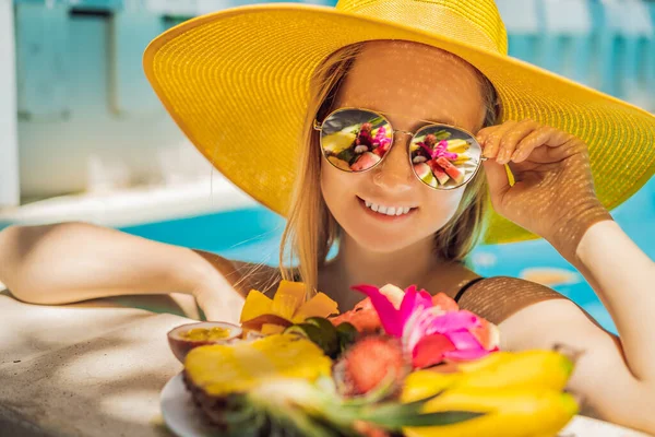 Mujer joven relajándose y comiendo plato de frutas junto a la piscina del hotel. Dieta exótica de verano. Foto de piernas con comida sana junto a la piscina, vista superior desde arriba. Estilo de vida de playa tropical — Foto de Stock