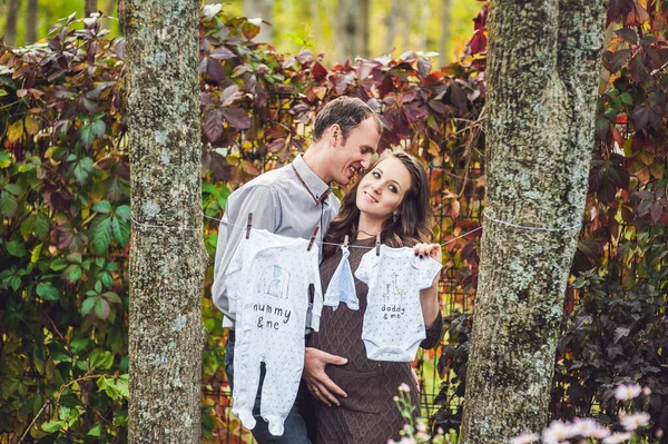 Une jeune femme enceinte et son mari. Une famille heureuse accrochant des vêtements de bébé pour sécher sur une corde. femme enceinte se détendre dans le parc . — Photo