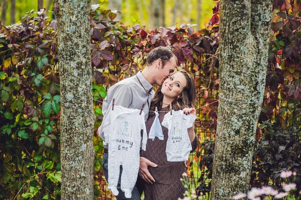 Беременная молодая женщина с мужем. Счастливая семья вешает детскую одежду на веревку. беременная женщина отдыхает в парке . — стоковое фото
