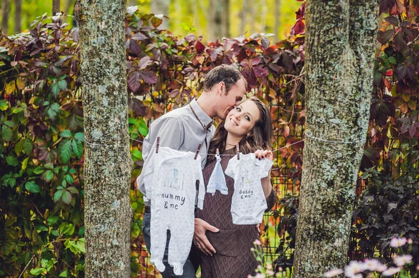 Une jeune femme enceinte et son mari. Une famille heureuse accrochant des vêtements de bébé pour sécher sur une corde. femme enceinte se détendre dans le parc . — Photo