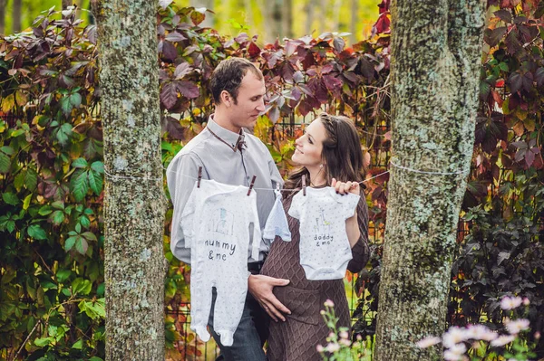 Une jeune femme enceinte et son mari. Une famille heureuse accrochant des vêtements de bébé pour sécher sur une corde. femme enceinte se détendre dans le parc . — Photo