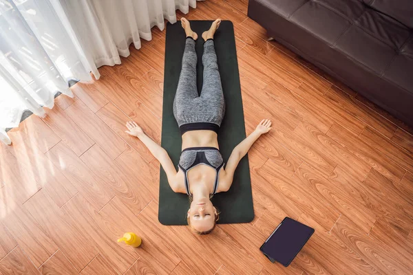 Donna fitness che si allena sul pavimento a casa e guarda i video di fitness in un tablet. La gente fa sport online a causa del coronovirus — Foto Stock