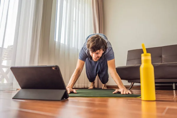 Fitness man exercising on the floor at home and watching fitness videos in a tablet. People do sports online because of the coronovirus — Stock Photo, Image