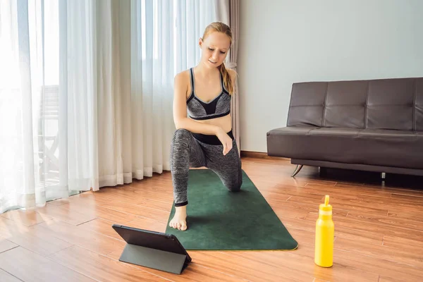 Mujer fitness haciendo ejercicio en el suelo en casa y viendo videos de fitness en una tableta. La gente hace deportes en línea debido al coronovirus — Foto de Stock