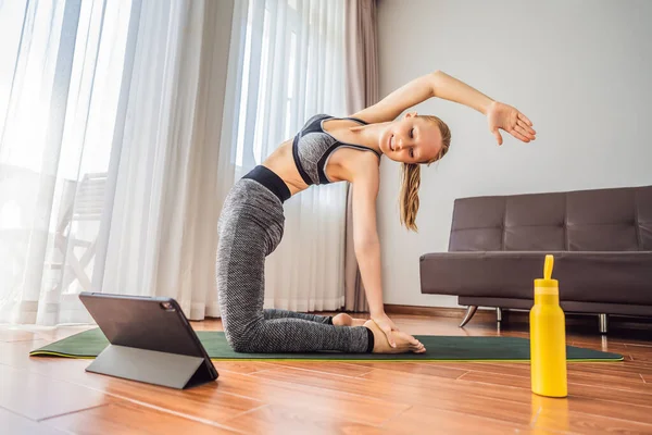 Fitness woman exercising on the floor at home and watching fitness videos in a tablet. People do sports online because of the coronovirus — Stock Photo, Image