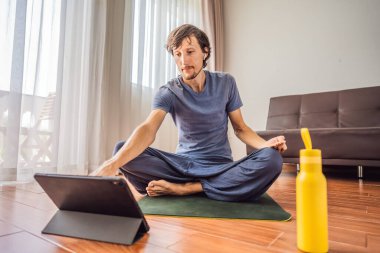 Spor salonundaki adam evde egzersiz yapıyor ve tablette spor videoları izliyor. İnsanlar koronovirüs yüzünden spor yapıyor.