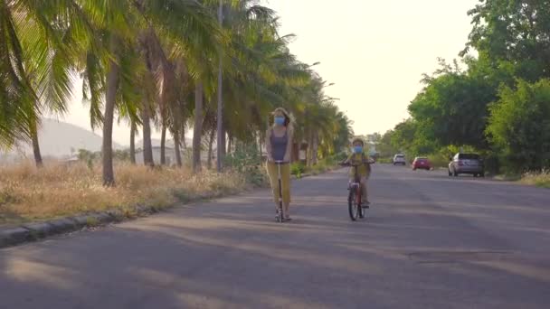 Aktywny chłopiec ze szkoły i jego mama jadą na rowerze i skuterze z plecakiem w słoneczny dzień. Szczęśliwe dziecko na rowerze w drodze do szkoły. Bezpieczna droga dla dzieci na zewnątrz do szkoły. Szkoły są otwarte po zamknięciu. — Wideo stockowe