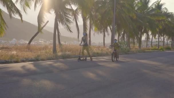 阳光明媚的日子，积极的学童男孩和他的妈妈骑自行车和摩托车背着背包。快乐的孩子骑自行车上学的路上。让孩子们在户外上学的安全方法。关了门后学校就开学了 — 图库视频影像