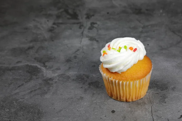Doces Cupcakes com cobertura de creme e polvilhas de arco-íris em cinza — Fotografia de Stock