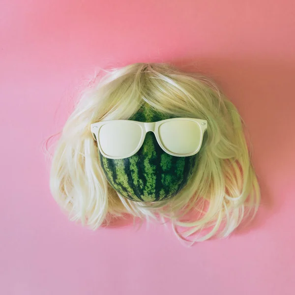 watermelon with blonde wig and white sunglasses on pink background..