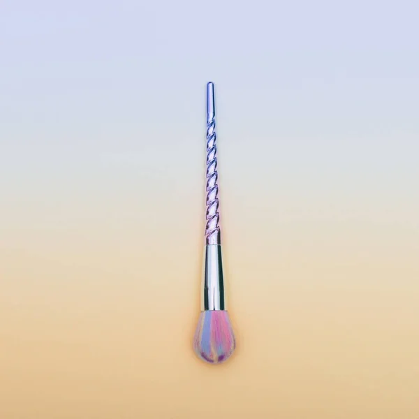 makeup brush shaped of a unicorn horn on gradient yellow and blue background