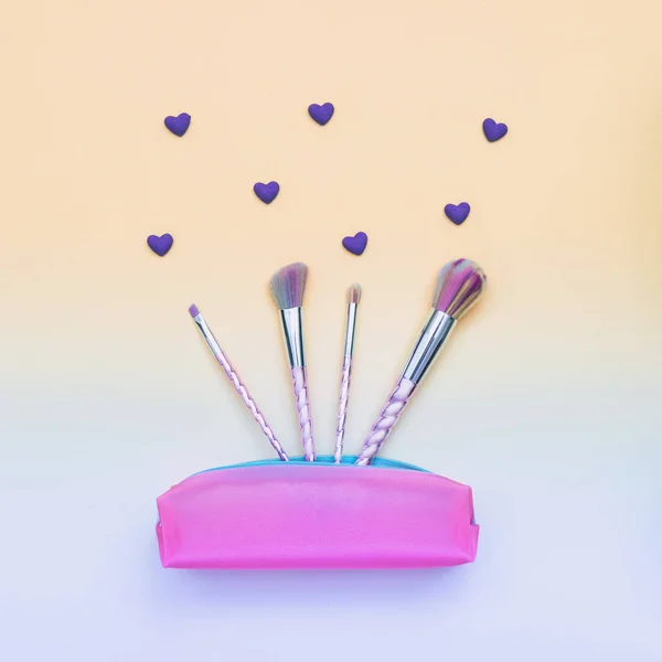 fashion colored makeup brushes in pink purse with hearts on gradient yellow and blue background