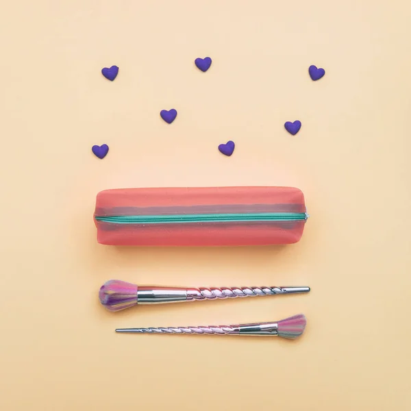 makeup brushes shaped of unicorn horn in pink purse with hearts on yellow background