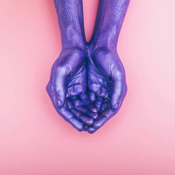 painted pearly purple hands are stacked together on pink background. palms up. minimal fashion concept