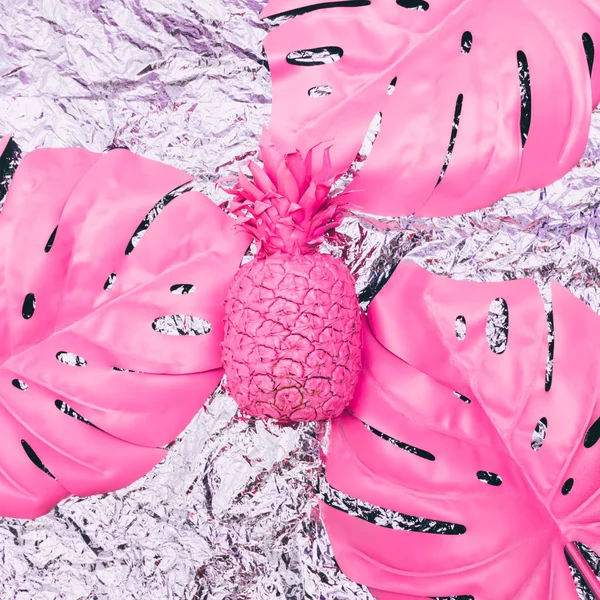 Painted pink pineapple with tropical palm leaves on metal foil.