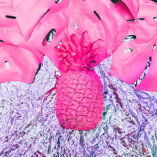 Painted pink pineapple with tropical palm leaves on metal foil.