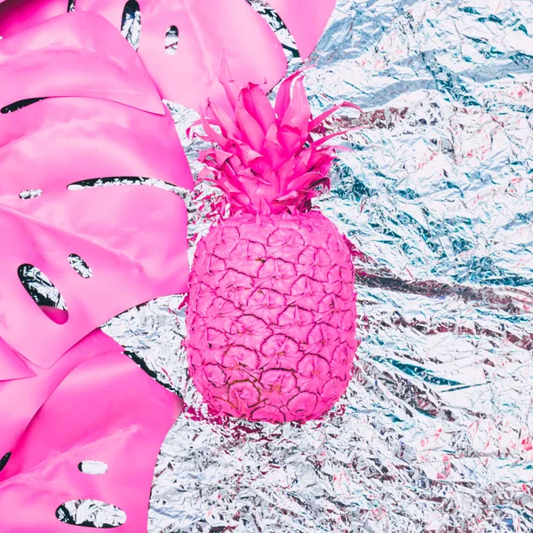 Painted pink pineapple with tropical palm leaves on metal foil.