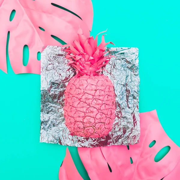 Painted pink pineapple with tropical palm leaves on metal foil and green background.