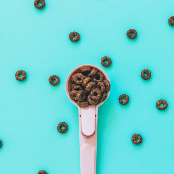 chocolate round cornflakes rings in pink measuring spoon, minimal art food for breakfast