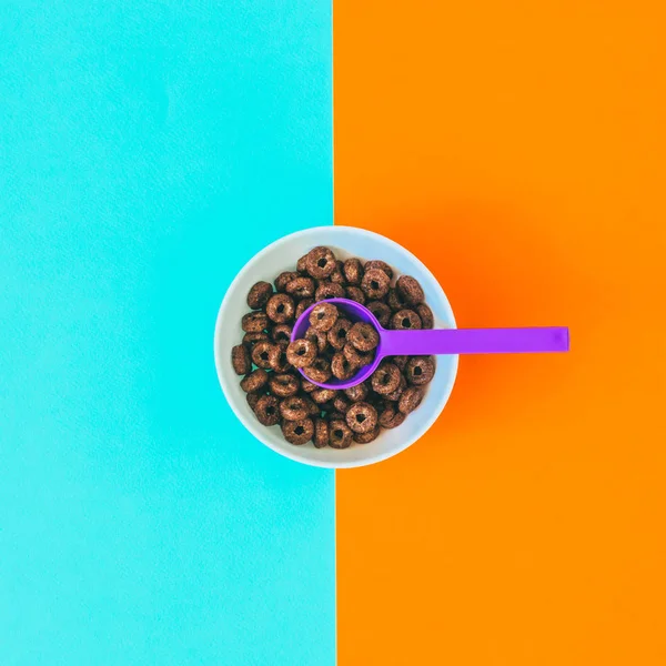 chocolate round cornflakes in white plate and purple spoon, creative breakfast