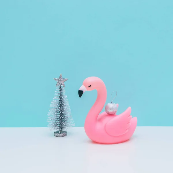 Silver decoration ball on plastic pink flamingo bird and fir tree on white and light blue background. Christmas and new year concept. Winter holidays composition.