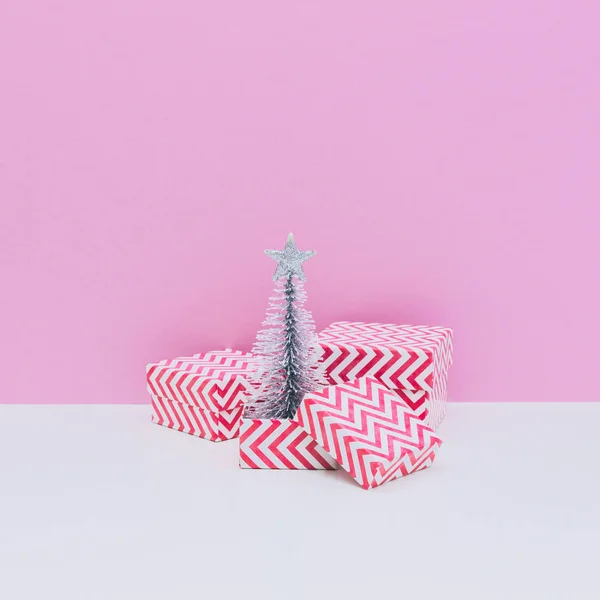 Silver fir tree among three sized gift boxes on white and light pink background. Christmas and new year concept. Winter holidays composition.