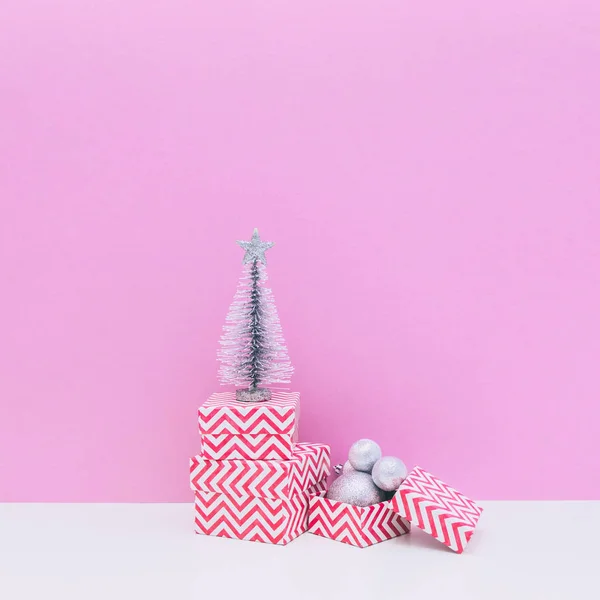 Winter holidays composition. Three sized gift boxes, decoration balls and fir tree on white and light pink background. Christmas and new year concept.