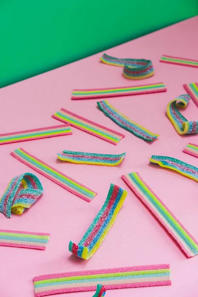 Rainbow chewable candy gums on pink and green background. Flat lay, top view.