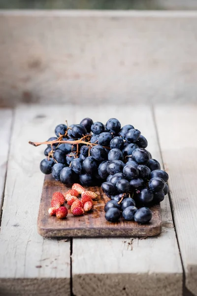 Bando de uvas azuis maduras e morangos silvestres em umas costas de madeira — Fotografia de Stock