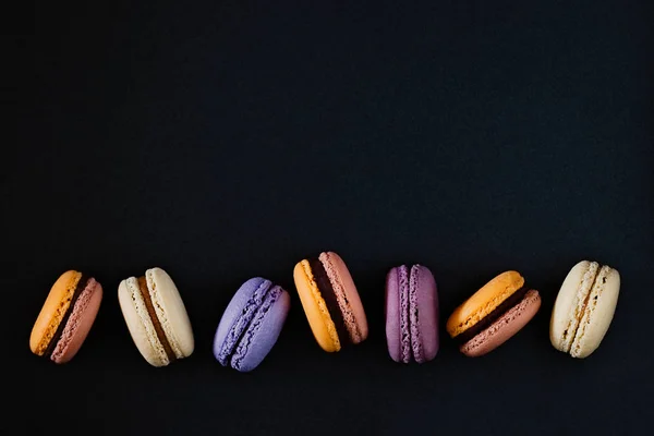 Macaroons ฝรั่งเศสที่มีสีสันบนพื้นหลังที่มืด . — ภาพถ่ายสต็อก