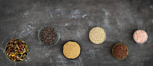Various superfoods on a dark grey background.  Pistachios, chia seeds, amaranth, quinoa,  flex seeds, rose salt.