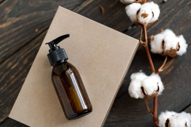 Koyu kahverengi cam kozmetik şişesi ve kağıt el işi kutusu.