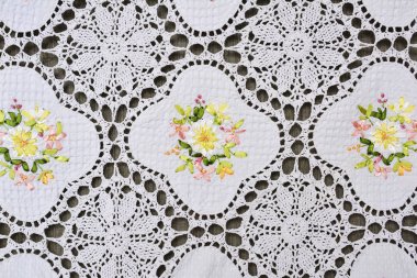 Multi-colored ornate floral pattern on white cotton lace tablecl clipart