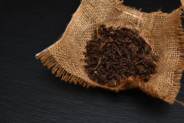 Une poignée de feuilles de thé sèches sur une planche, une assiette ou un plateau en ardoise noire. T — Photo
