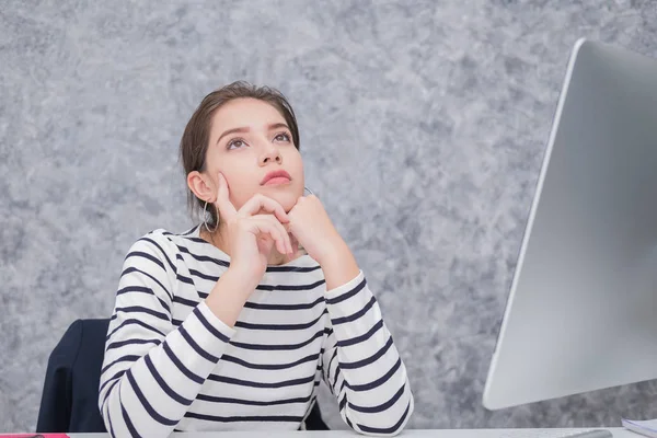 Mulher bonita olhando para uma tela de computador e pensando no escritório — Fotografia de Stock